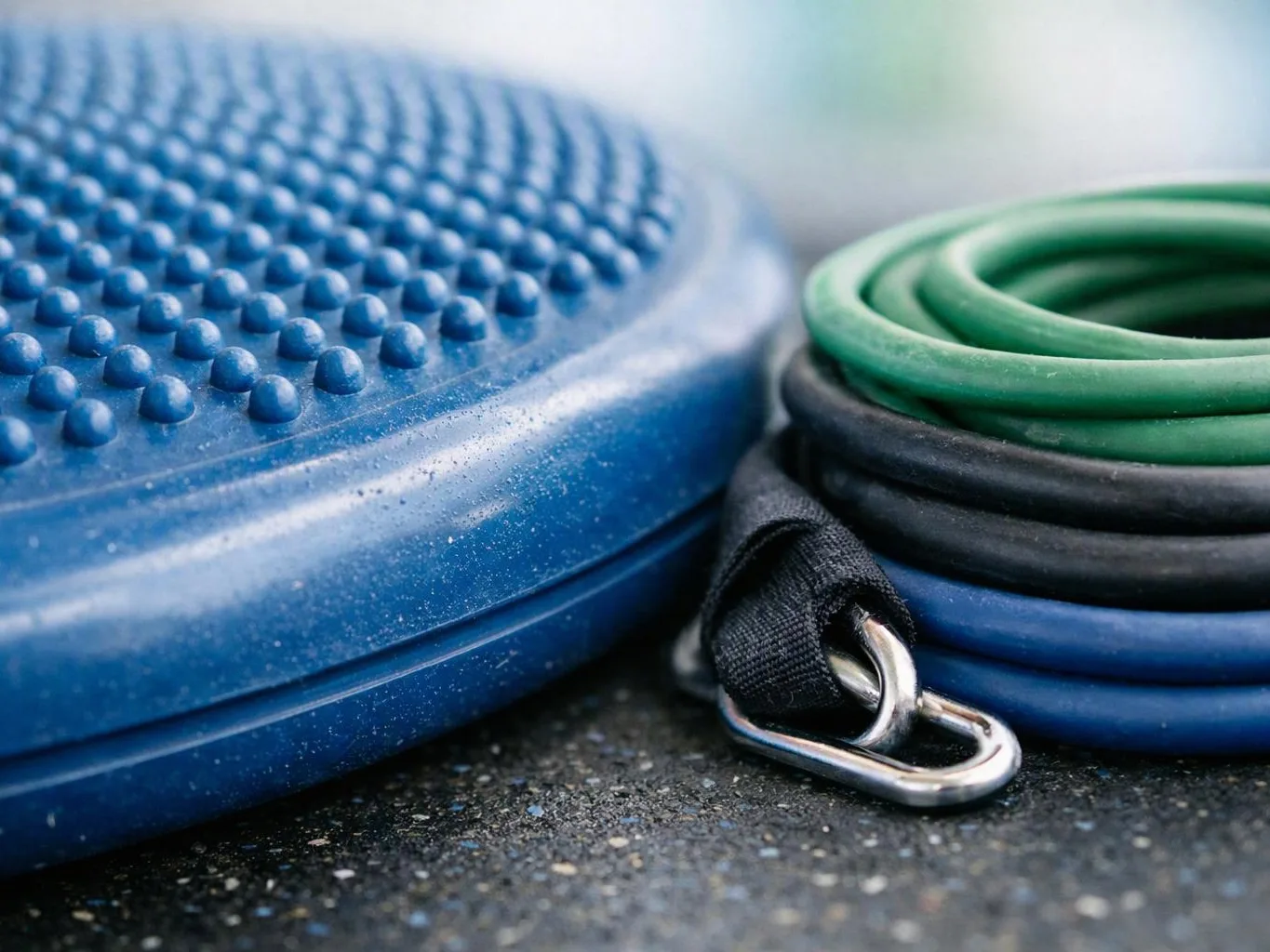 A blue textured balance disc sits beside rolled green and black resistance bands on a floor