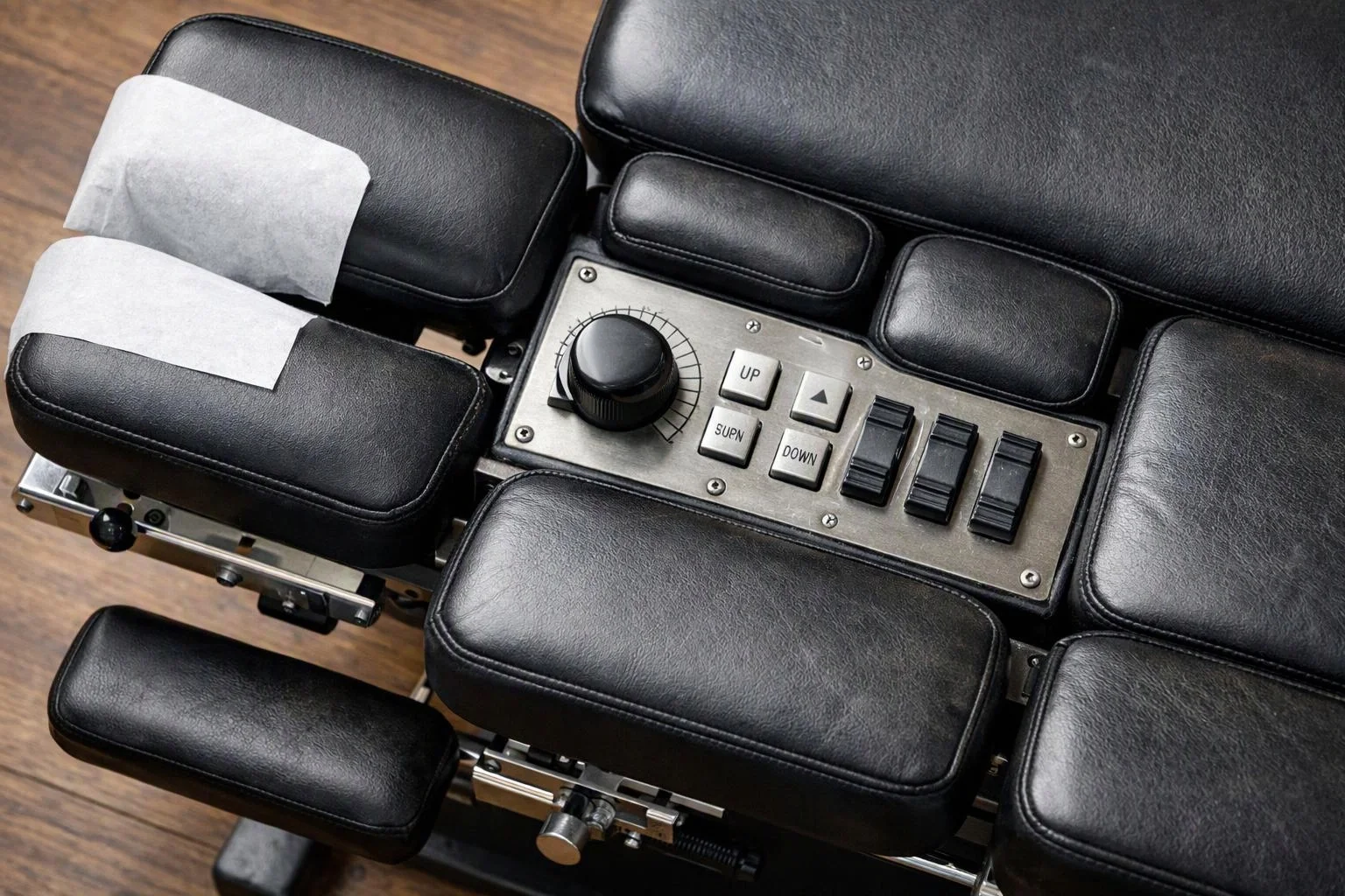 A black padded control chair shows a central metal panel with switches and a large knob on a wood floor